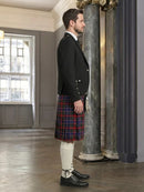 Man wearing a black jacket and red plaid kilt in an elegant room with marble columns.