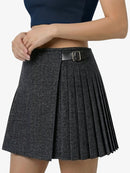 Person wearing a pleated skirt with a belt on a plain background