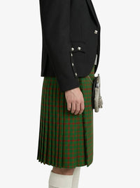 Person wearing a black blazer and green plaid kilt on a white background