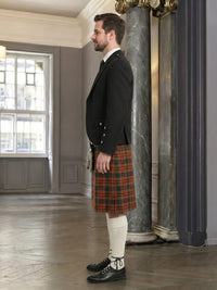 Man in formal attire with a kilt standing in an elegant room.