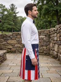 A man in a white dress shirt and black bow tie stands in profile outdoors wearing a kilt with an American flag pattern featuring red and white stripes and a blue panel with white stars.