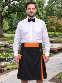A man wearing a black kilt with bright orange side panels and a matching orange waistband, paired with a white dress shirt and black bow tie, standing outdoors in a garden setting.