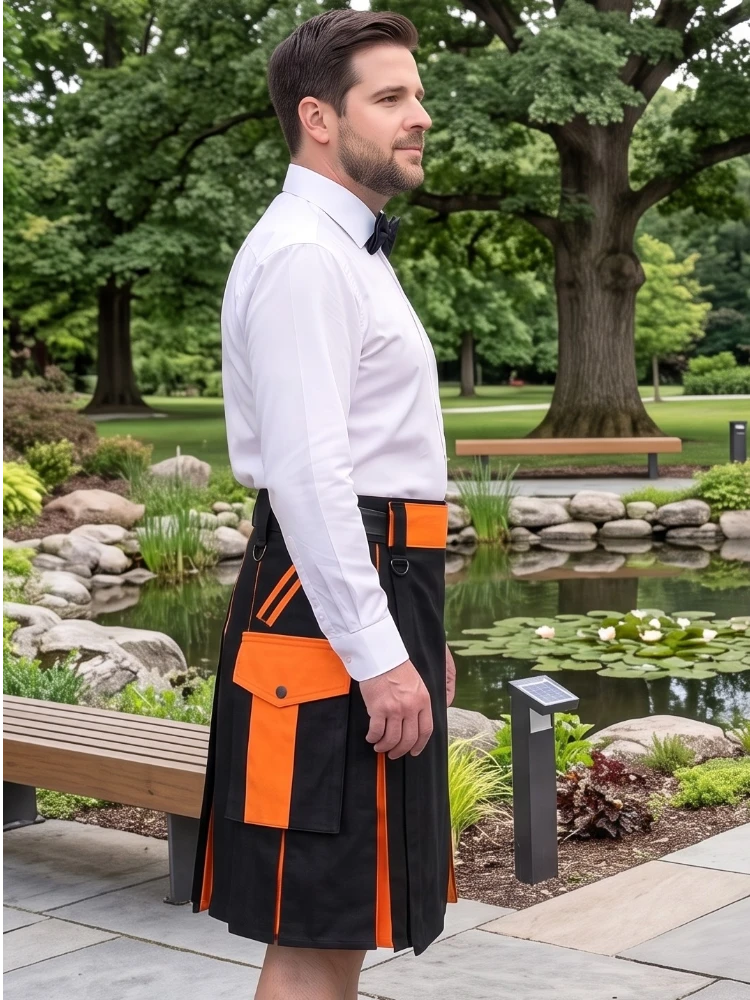 A man wearing a black kilt with bright orange accents and a white dress shirt stands in a park next to a pond with trees in the background.