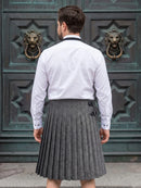 A man viewed from behind wearing a white long-sleeve dress shirt and a gray pleated herringbone kilt, standing in front of a large dark green ornate door with lion head knobs.
