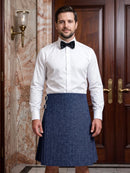 A man wearing a white dress shirt, black bow tie, and a blue pleated kilt stands in front of a dark wood door and marble wall.