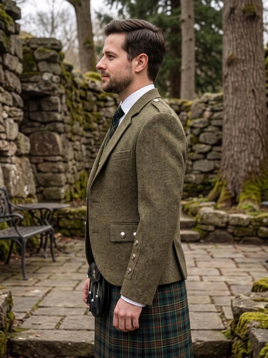 A man in profile wearing a brown tweed blazer and a green tartan kilt, standing outdoors in a stone garden setting.