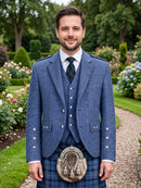 A man standing in a formal garden wearing a blue Scottish formalwear outfit with a kilt, sporran, tie, and blazer.