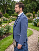 A man standing in profile in a formal garden, wearing a blue herringbone blazer, a blue plaid kilt, a white shirt, and a dark tie, with a sporran at his side.