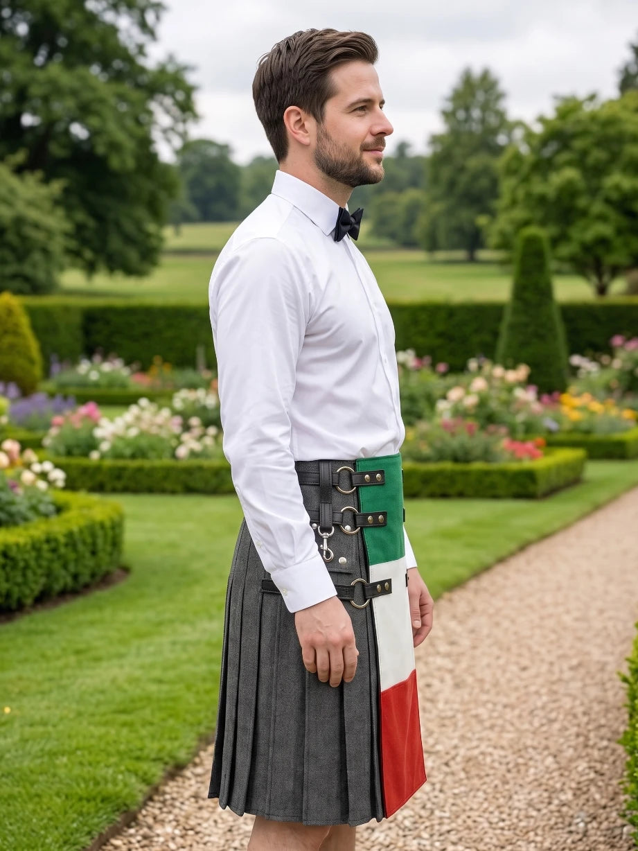 A man standing in a garden wearing a gray pleated kilt with a green, white, and red vertical panel on the back, a white dress shirt, and a black bow tie.