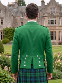 A man viewed from behind wearing a bright green Scottish kilt jacket with silver buttons and a green and blue tartan kilt, standing in a garden with a large stone mansion in the background.