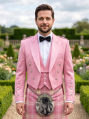 A man wearing a pink double-breasted formal jacket with silver buttons, a white shirt, a black bow tie, and a pink plaid kilt with a sporran, standing in a formal garden.