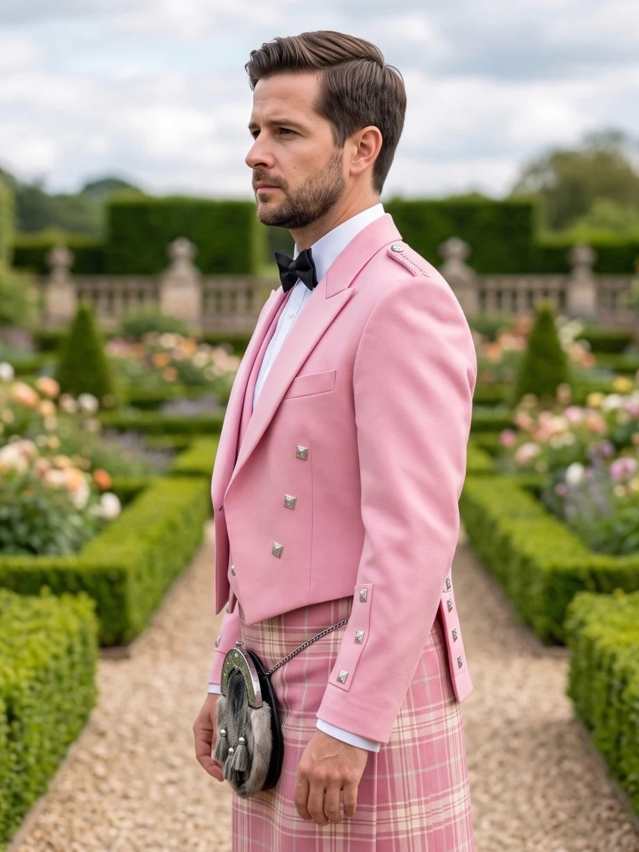 A man in a formal garden wearing a pink double-breasted blazer, a pink plaid kilt, a white shirt, and a black bow tie, holding a black sporran.