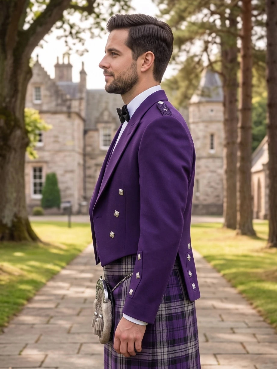 A man in profile wearing a formal purple kilt jacket with silver buttons, a purple tartan kilt, a white shirt, and a black bow tie, standing outdoors on a stone path with a castle and trees in the background.