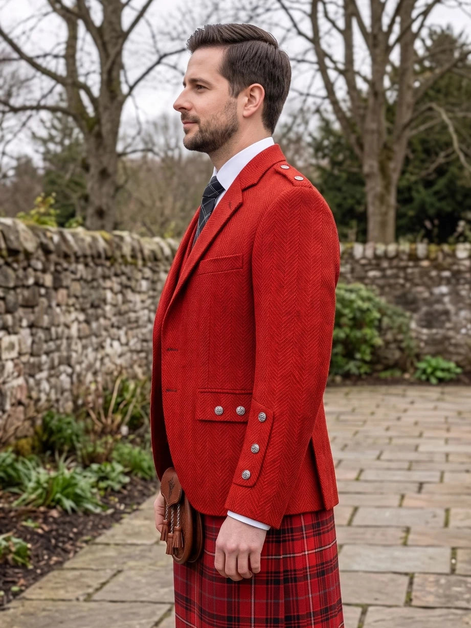 A man in profile wearing a bright red kilted jacket and a red tartan kilt, standing outdoors on a stone path with a stone wall and bare trees in the background.