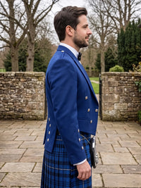 A man in profile wearing a royal blue Scottish kilt suit with silver buttons, a white shirt, and a blue tartan kilt, standing outdoors on a stone patio.