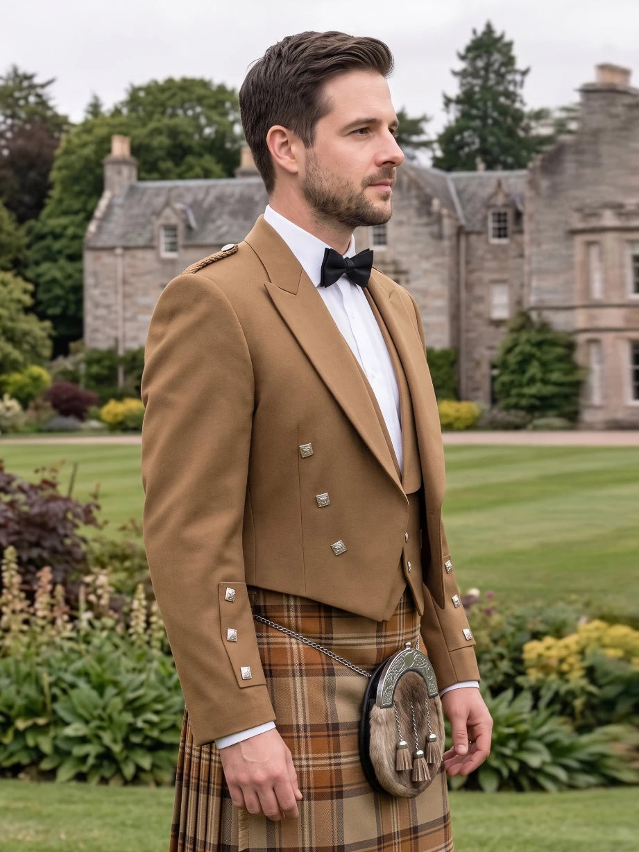 A man wearing a traditional Scottish formal outfit with a tan double-breasted jacket, white shirt, black bow tie, and a brown plaid kilt with a sporran, standing in a garden with a stone mansion in the background.