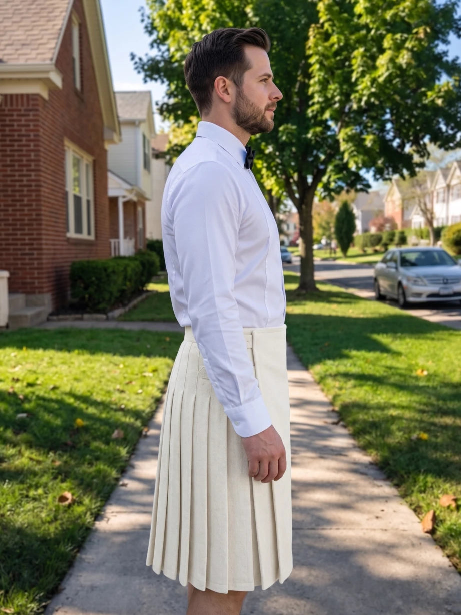 A man wearing a white long-sleeve dress shirt and a pleated cream-colored kilt stands on a suburban sidewalk, shown in profile against a background of houses, trees, and grass.