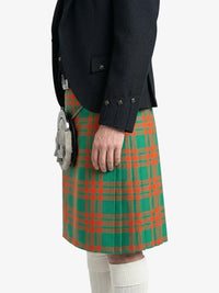 Person wearing a green and red plaid kilt with a black jacket on a white background