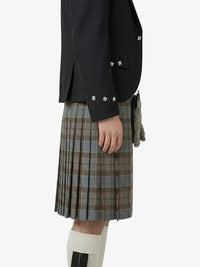 Person wearing a black jacket and plaid kilt on a white background