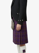 Person wearing a black blazer and purple plaid kilt on a white background
